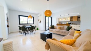 A modern living room with a sofa, dining table, and chairs. There is a kitchen area with cabinets and a countertop. - Residence Jannet 1 Luxury Seaside 3 Bedrooms (Hammamet)
