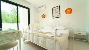 Une chambre à coucher avec un lit blanc, une table de chevet, une chaise, une fenêtre et un climatiseur fixé au mur.