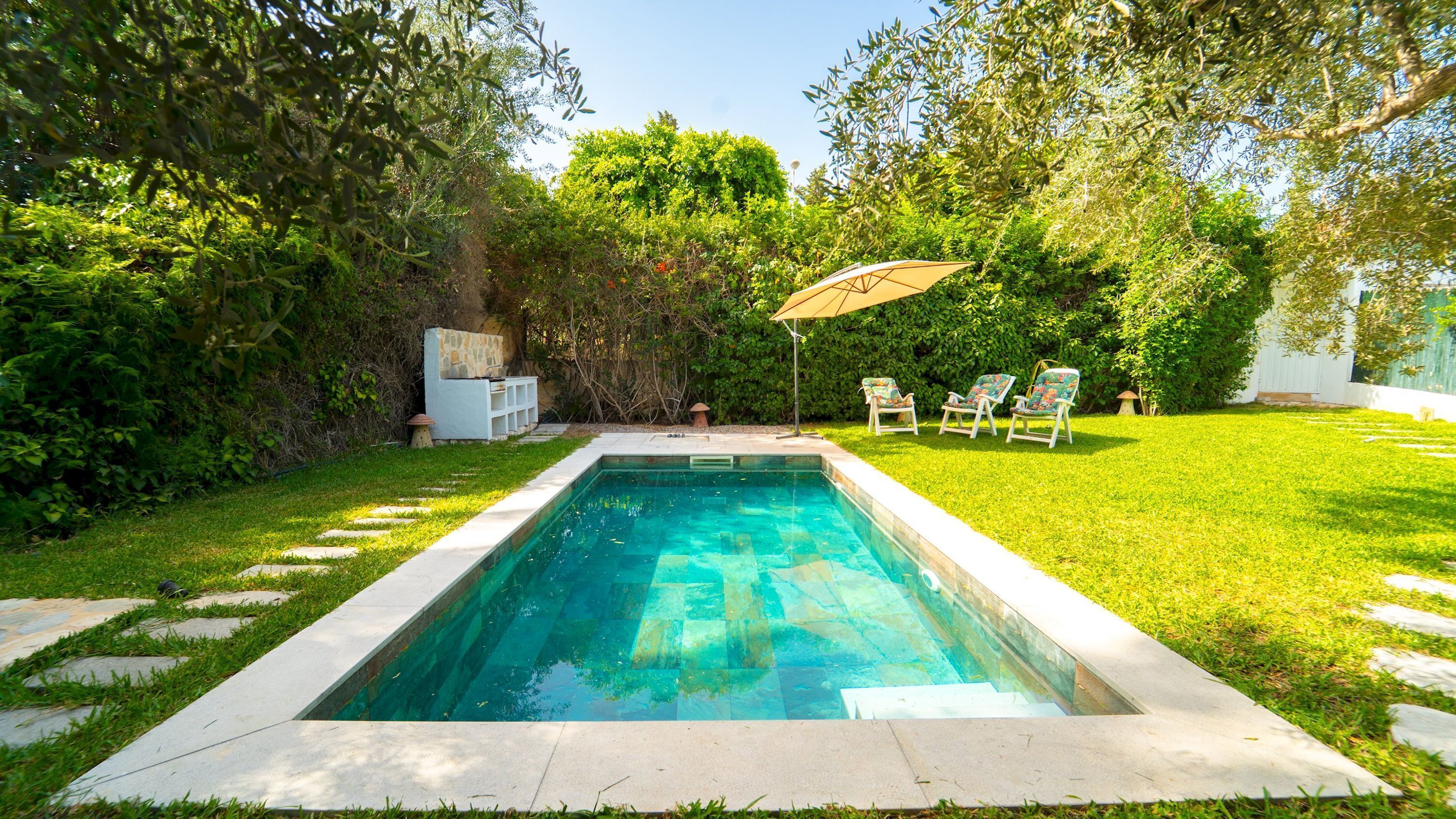 A rectangular swimming pool with a stone border, surrounded by a well-maintained lawn and trees.