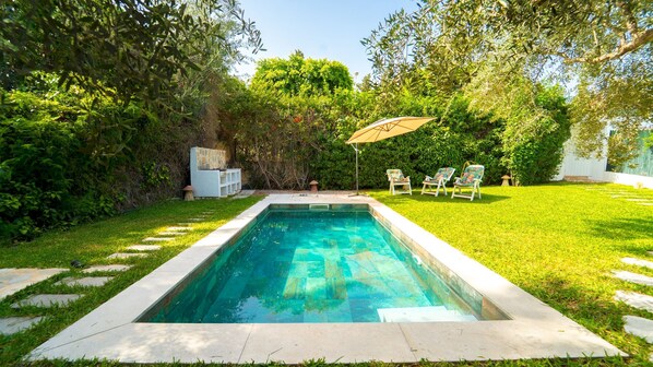Une piscine rectangulaire bordée de pierres, entourée d’une pelouse bien entretenue et d’arbres.