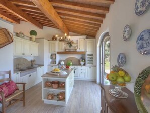 A kitchen with white cabinets, copper cookware, a wooden bench, and a fruit bowl. - Villa Torresassa with Private Pool (Montaione)
