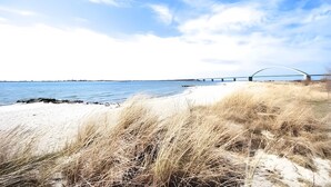 A beach with sand, grass, and a bridge over water. - Port on the Fehmarnsund – Sea View and Beach at Your Doorstep (Fehmarn)