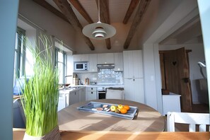 Une cuisine moderne avec des meubles blancs, un plafond en bois et une table à manger sur laquelle se trouve un plateau de fruits et de légumes.
