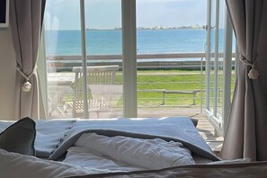 Ein Schlafzimmer mit großem Fenster und Meerblick, sowie einer Terrasse.