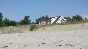A beach house with a sloped roof, a wooden door, and a fenced area. - Port on the Fehmarnsund – Sea View and Beach at Your Doorstep (Fehmarn)