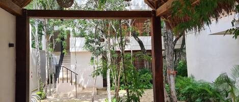 A covered outdoor area with a stone pathway, wooden pergola, hanging wicker lamps, and lush greenery.