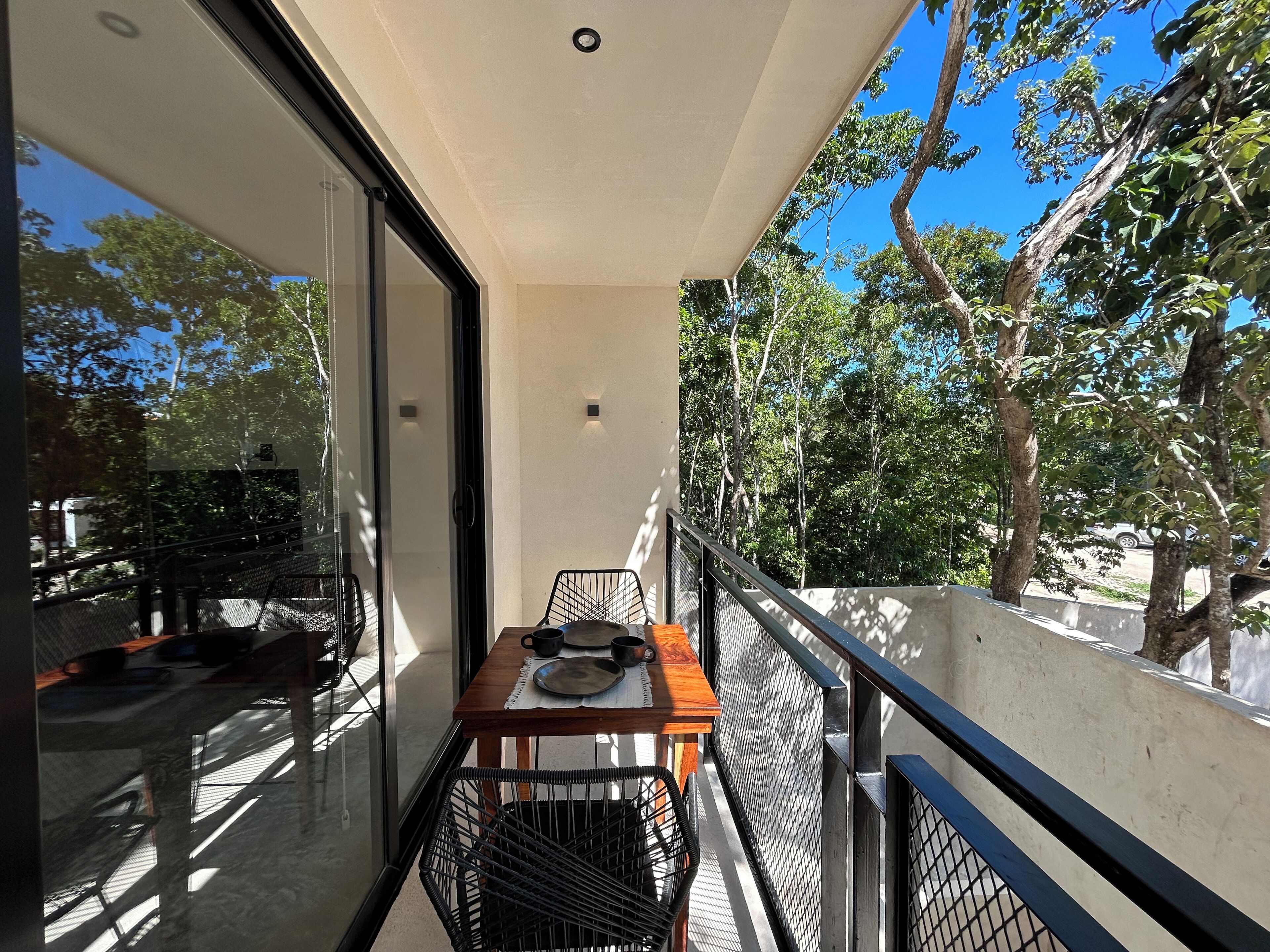 A balcony with a table, chairs, and a view of trees and a car.