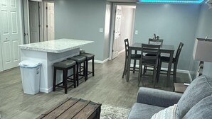 A modern living room with a grey sofa, a wooden chest, and a dining area with a table and chairs.