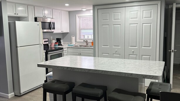 A modern kitchen with white cabinets, a large island with bar stools, and a stainless steel refrigerator.