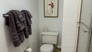 Une petite salle de bain comprenant des toilettes, un porte-serviettes avec des serviettes, un tableau encadré au mur et une poubelle.