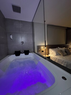 Ein modernes Badezimmer mit einer großen Badewanne, einem Spiegel und einem Bett mit einem Holz-Kopfteil.