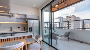 A modern kitchen with a built-in oven, a dining area with a wooden table and chairs, and a balcony with a view of the cityscape. - Hotel Time Oclock (Medellín)