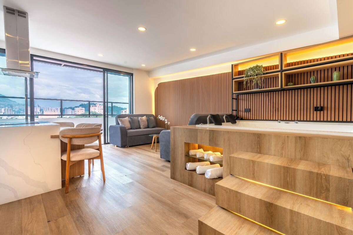 A modern hotel lobby with a wooden reception desk, seating area, and large windows offering a city view.