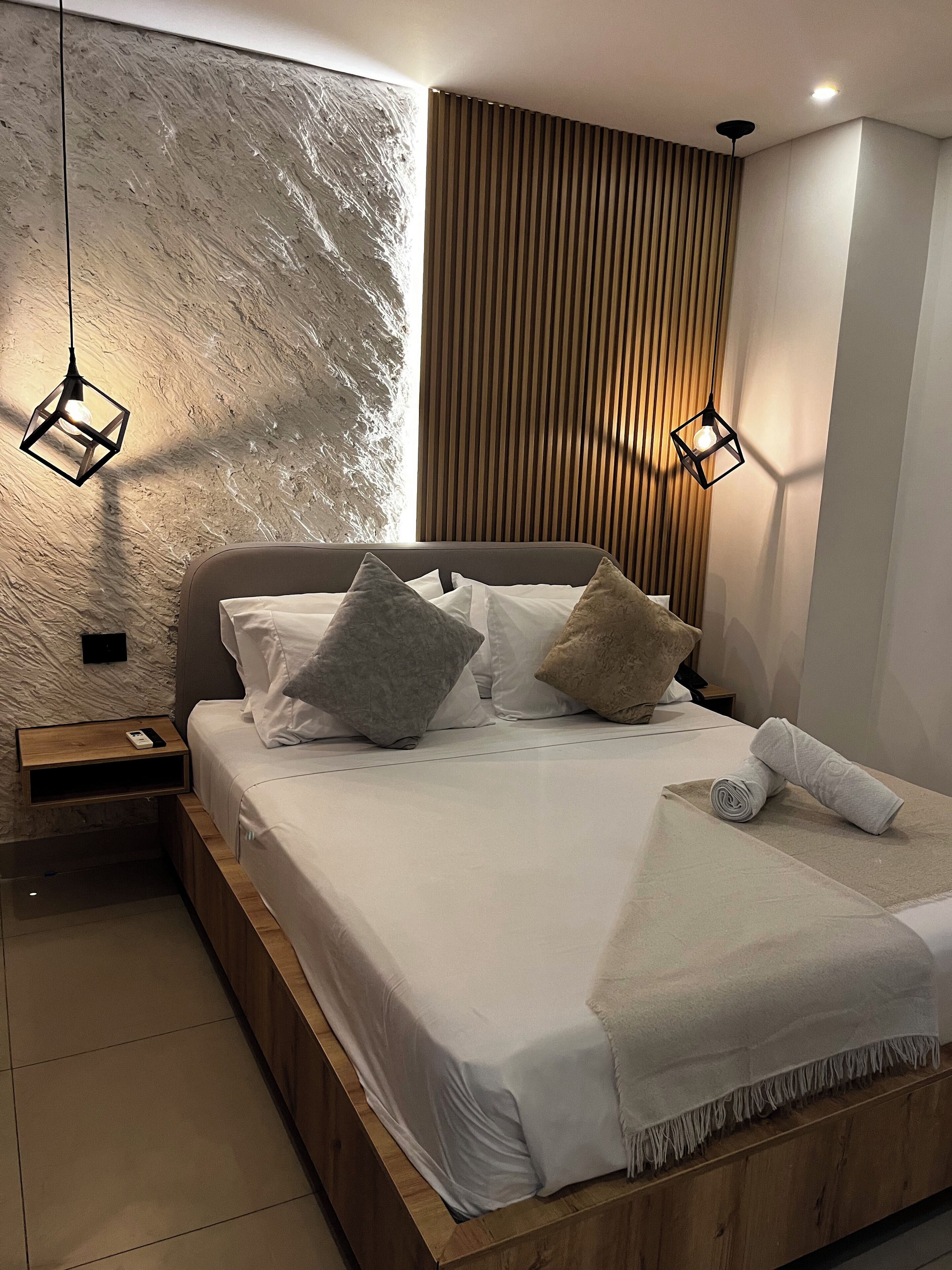 A modern bedroom with a wooden bed frame, white bedding, and two pendant lights.
