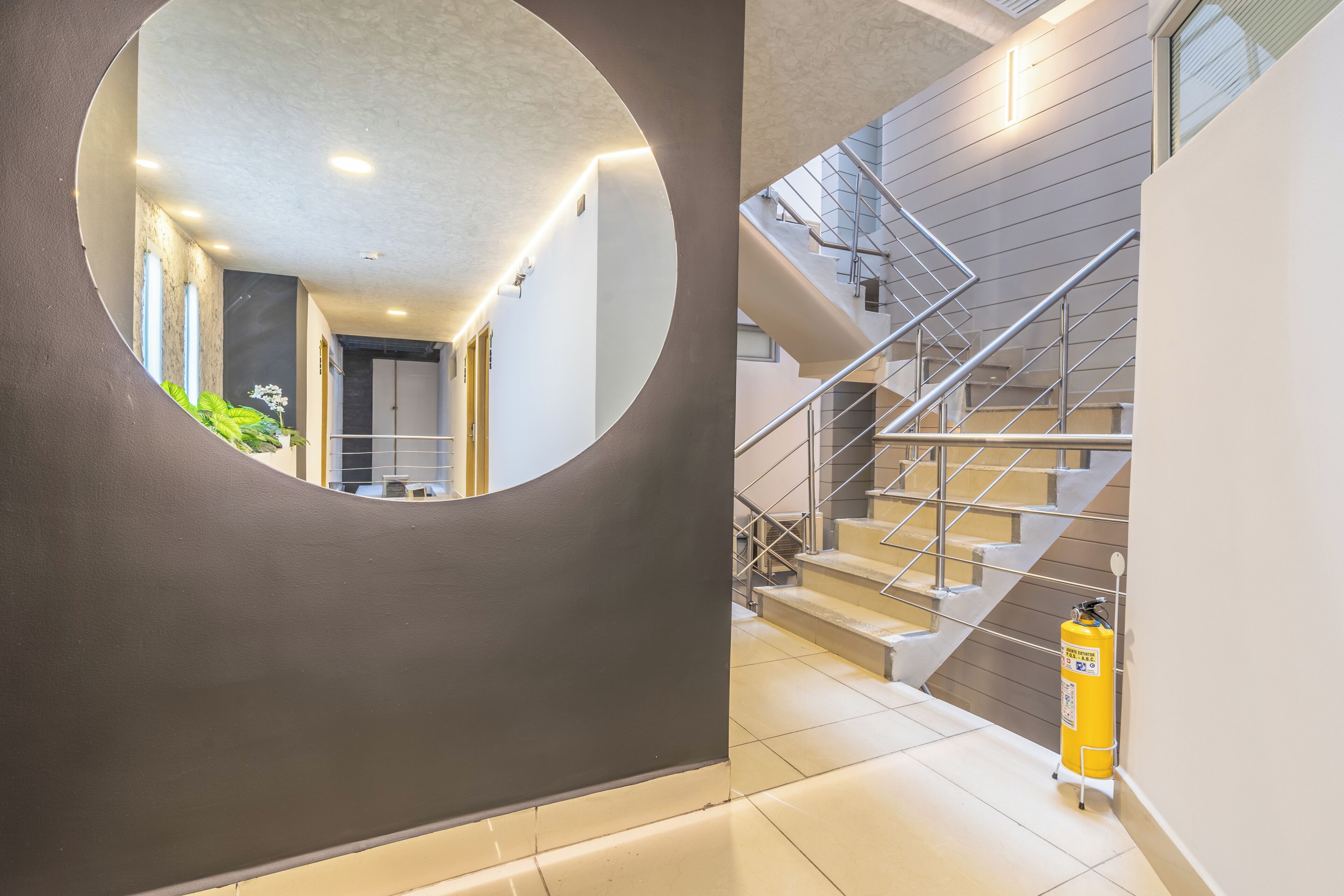 A modern interior with a circular mirror, a staircase, and a fire extinguisher.
