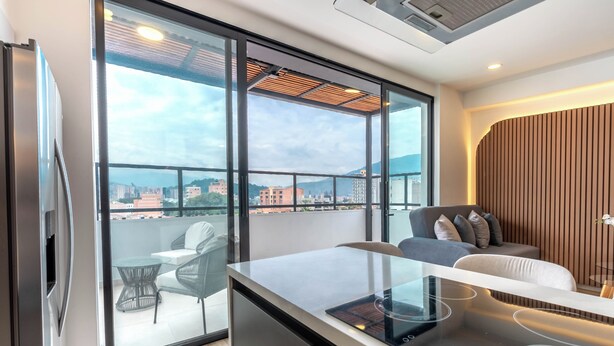 A modern kitchen with a large window, a dining area with a sofa, and a view of the cityscape. - Hotel Time Oclock (Medellín)
