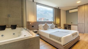 A modern hotel room with a large bed, a separate bathroom with a bathtub, a desk, and a view of the city. - Hotel Time Oclock (Medellín)