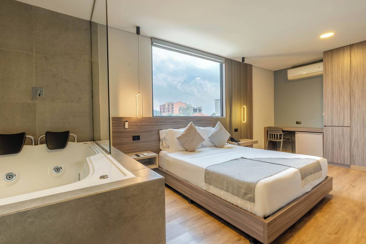A modern hotel room with a large bed, a separate bathroom with a bathtub, a desk, and a view of the city.