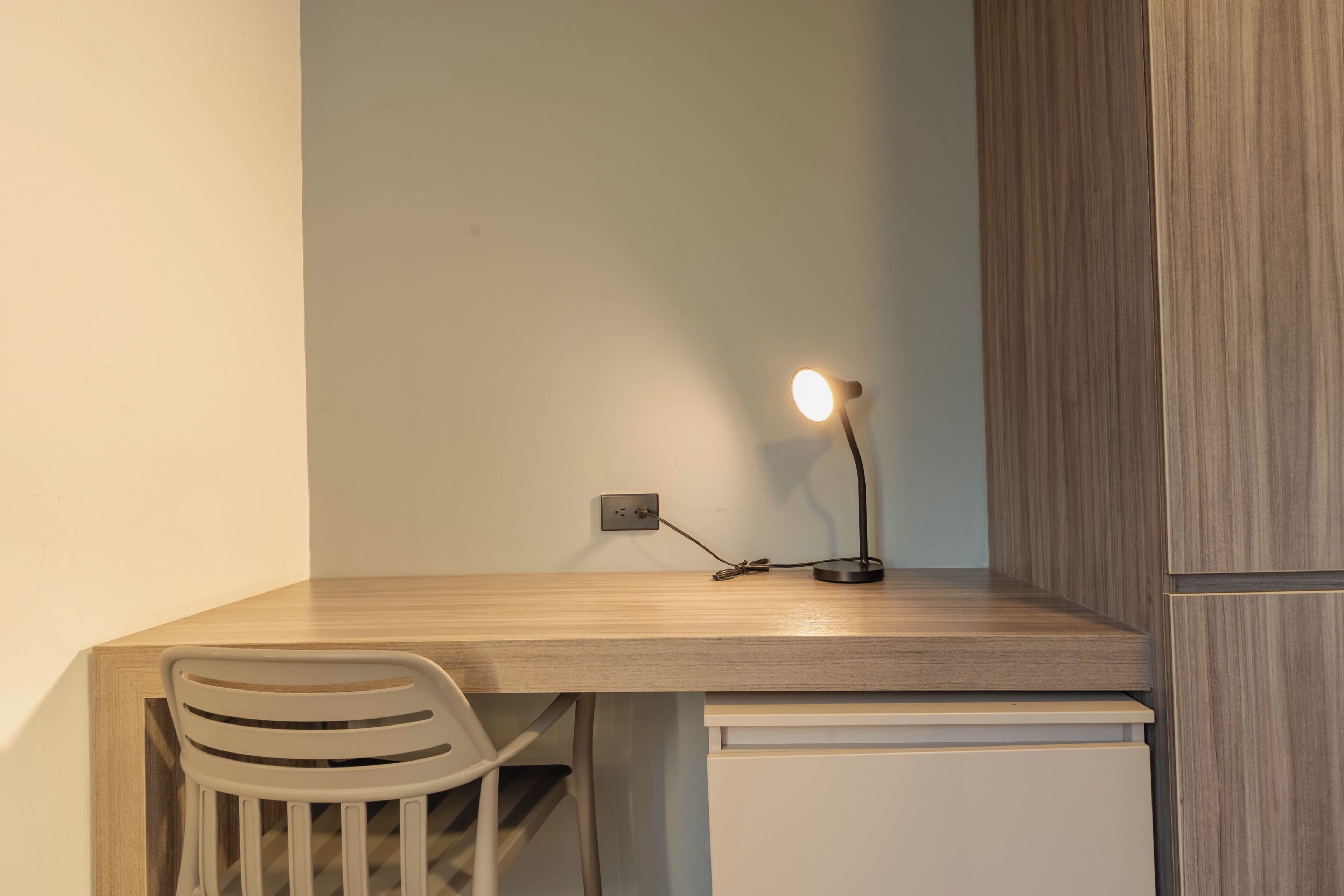 Ein Schreibtisch mit Stuhl und einer Schreibtischlampe, sowie ein weißes Schranksystem.