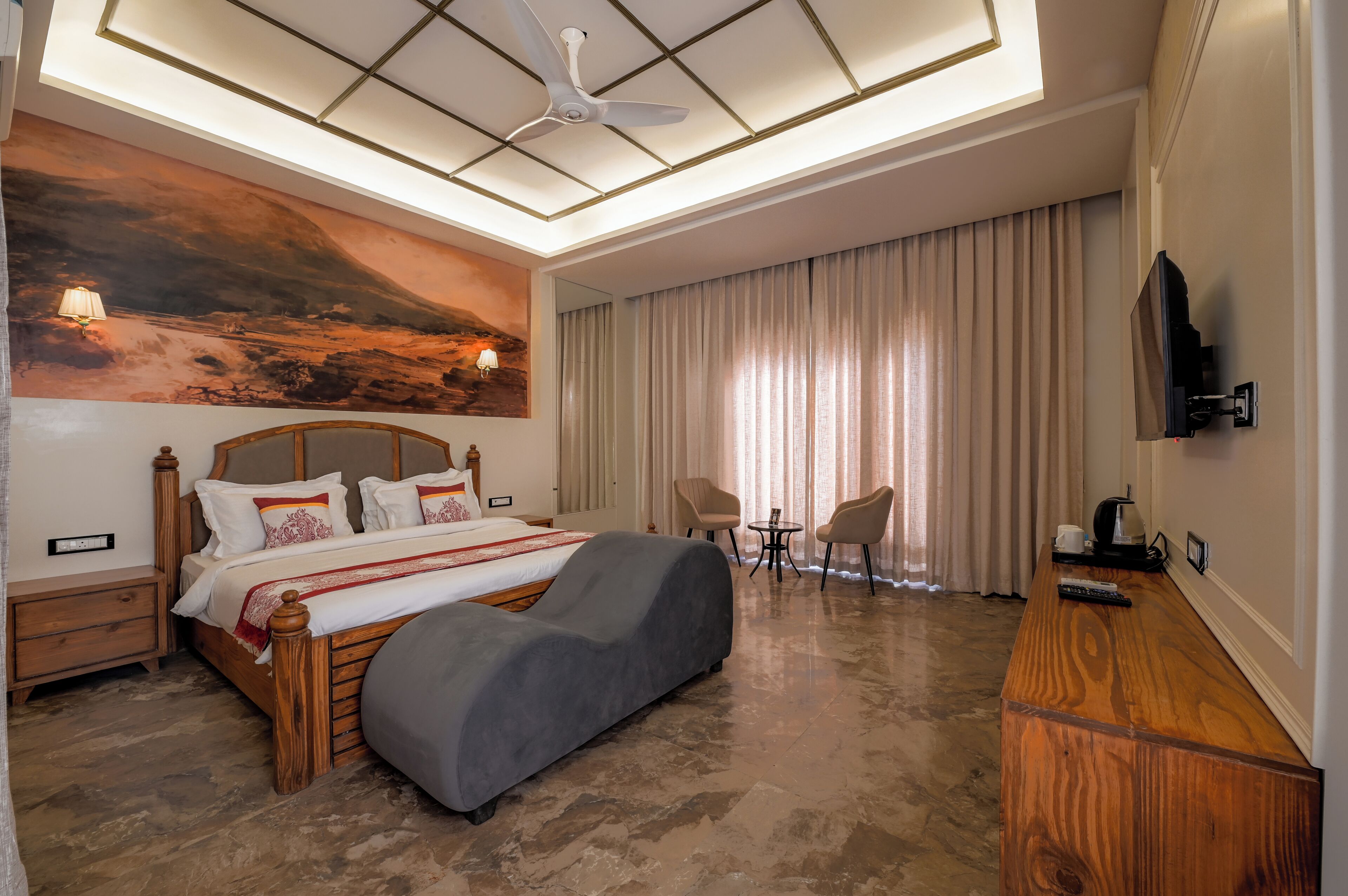 Habitación de hotel con una cama grande, ventilador de techo, televisor montado en la pared y un cuadro en la pared.