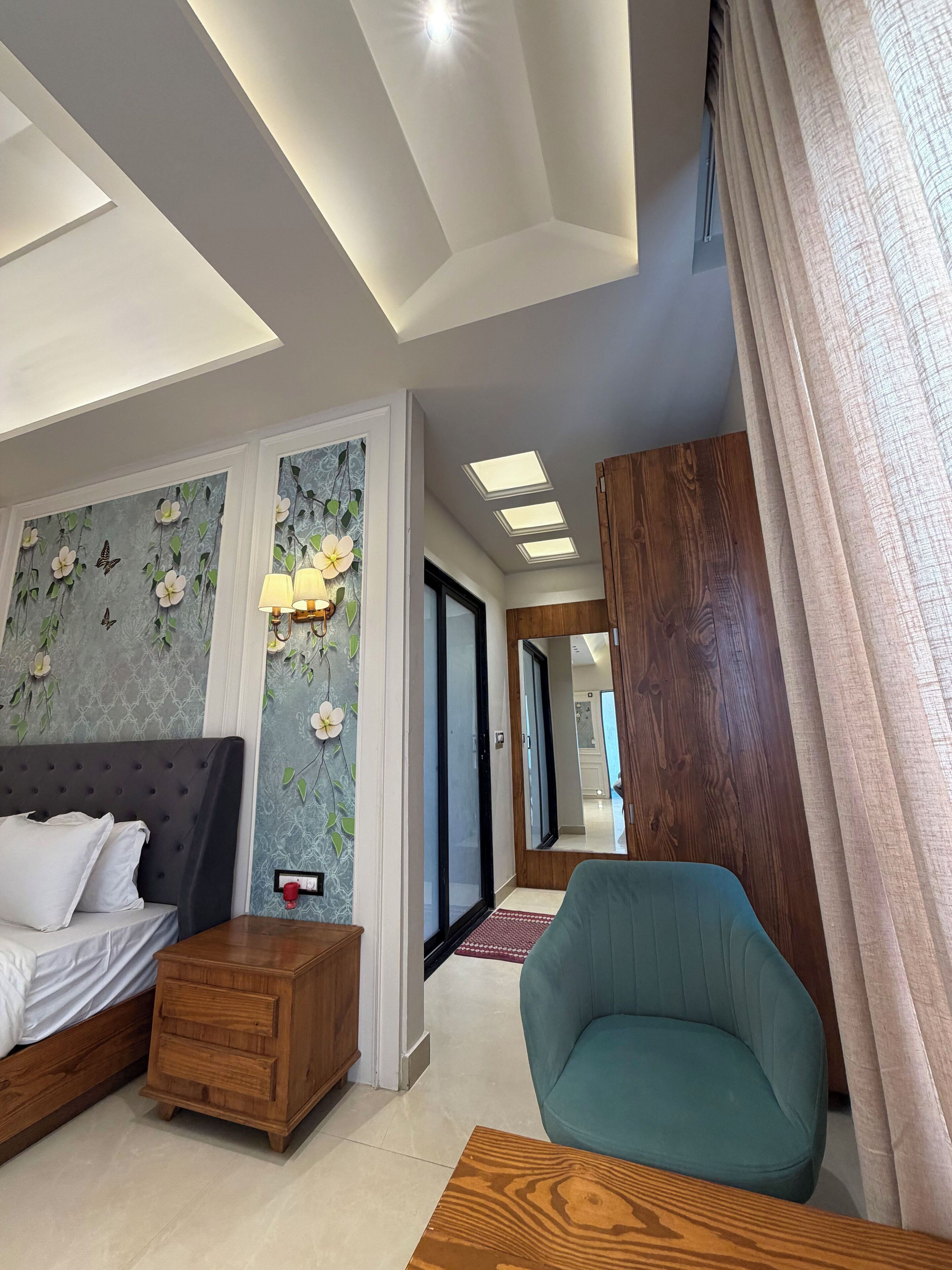 Una habitación de hotel moderna con una cama, una mesita de noche de madera, un sillón azul verdoso y una mesa de centro de madera.