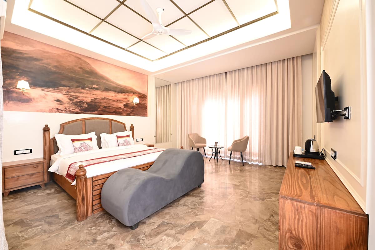 A modern hotel room with a large bed, a desk, a TV, and a painting on the wall.