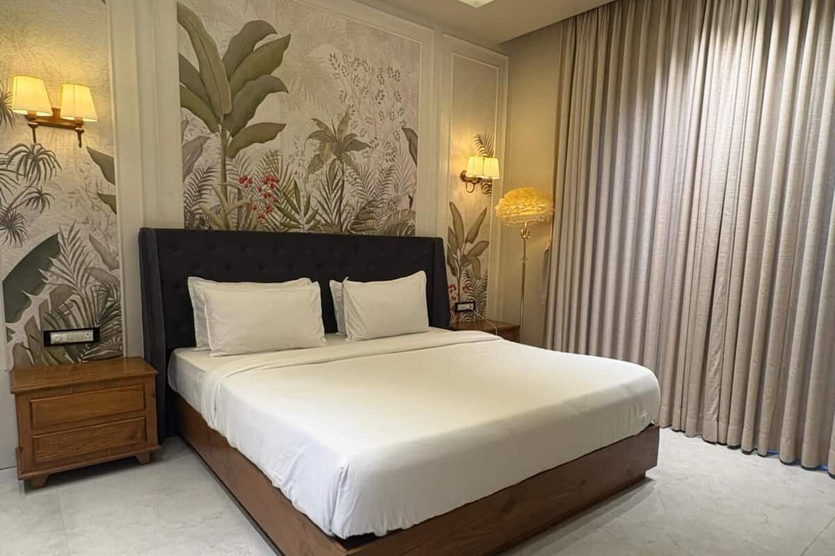 A neatly made bed with a wooden frame and white linens, a nightstand with a lamp, and a wall with a tropical mural.