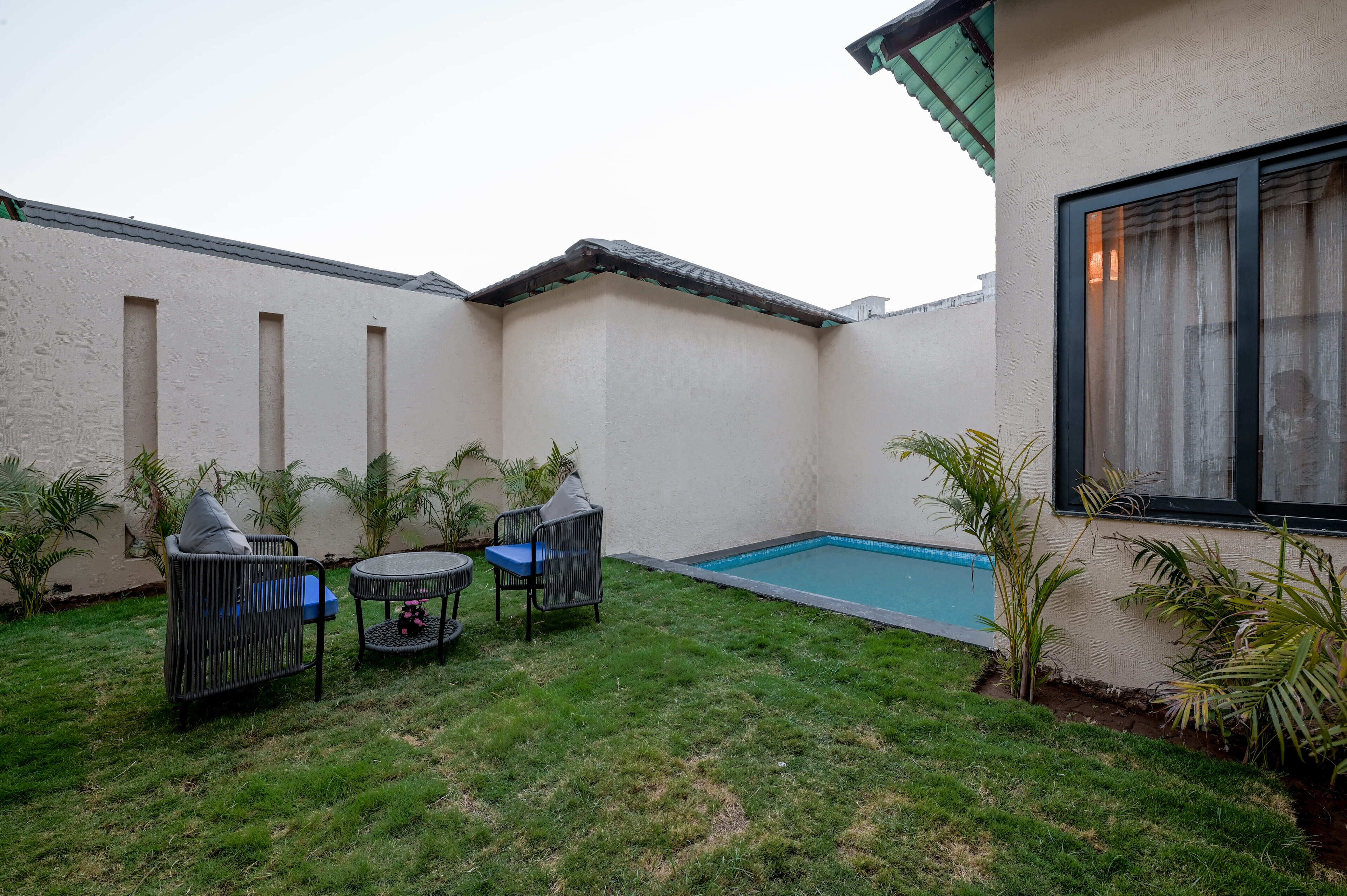 Un patio trasero con piscina, una pequeña mesa, dos sillas y plantas en macetas.