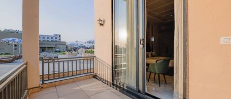A balcony with a glass door leading to a room with a table and chairs.