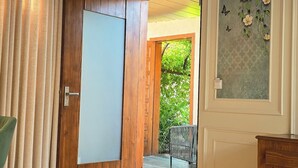 A bedroom with a large bed, wooden door, and a view of a garden through an open door. - The Bhagwati Cottage & Villa (Abu Road)