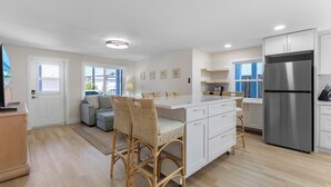 Une cuisine moderne avec des meubles blancs, un réfrigérateur en acier inoxydable et un coin repas doté de chaises en osier.