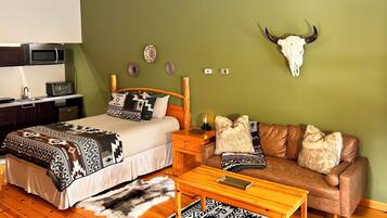 A room with a bed, a sofa, a coffee table, a wall-mounted microwave, a small table with a lamp, and a wall-mounted bull skull.