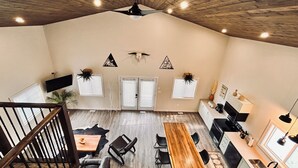 A spacious room with a high ceiling, wooden beams, a dining area with a long table and chairs, a kitchen with modern appliances, and decorative wall art. - Cow Lake Store and Resort (rocky mountain house)