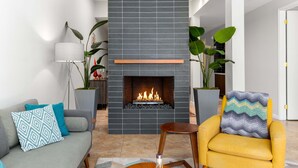 Una sala moderna con chimenea, un sofá, un sillón amarillo y plantas en macetas.