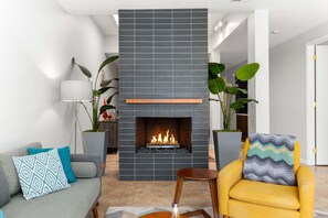 Una sala moderna con chimenea, un sofá, un sillón amarillo y plantas en macetas.