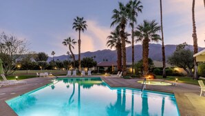 Una piscina con sillas de descanso, palmeras y montañas al fondo.