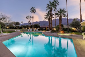 Una piscina con sillas de descanso, palmeras y montañas al fondo.