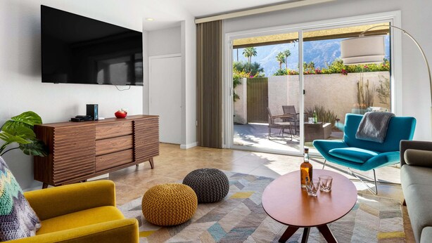 Una sala de estar moderna con un televisor de pantalla plana, un mueble de madera, un sillón amarillo, un sofá azul y una mesa de centro redonda.