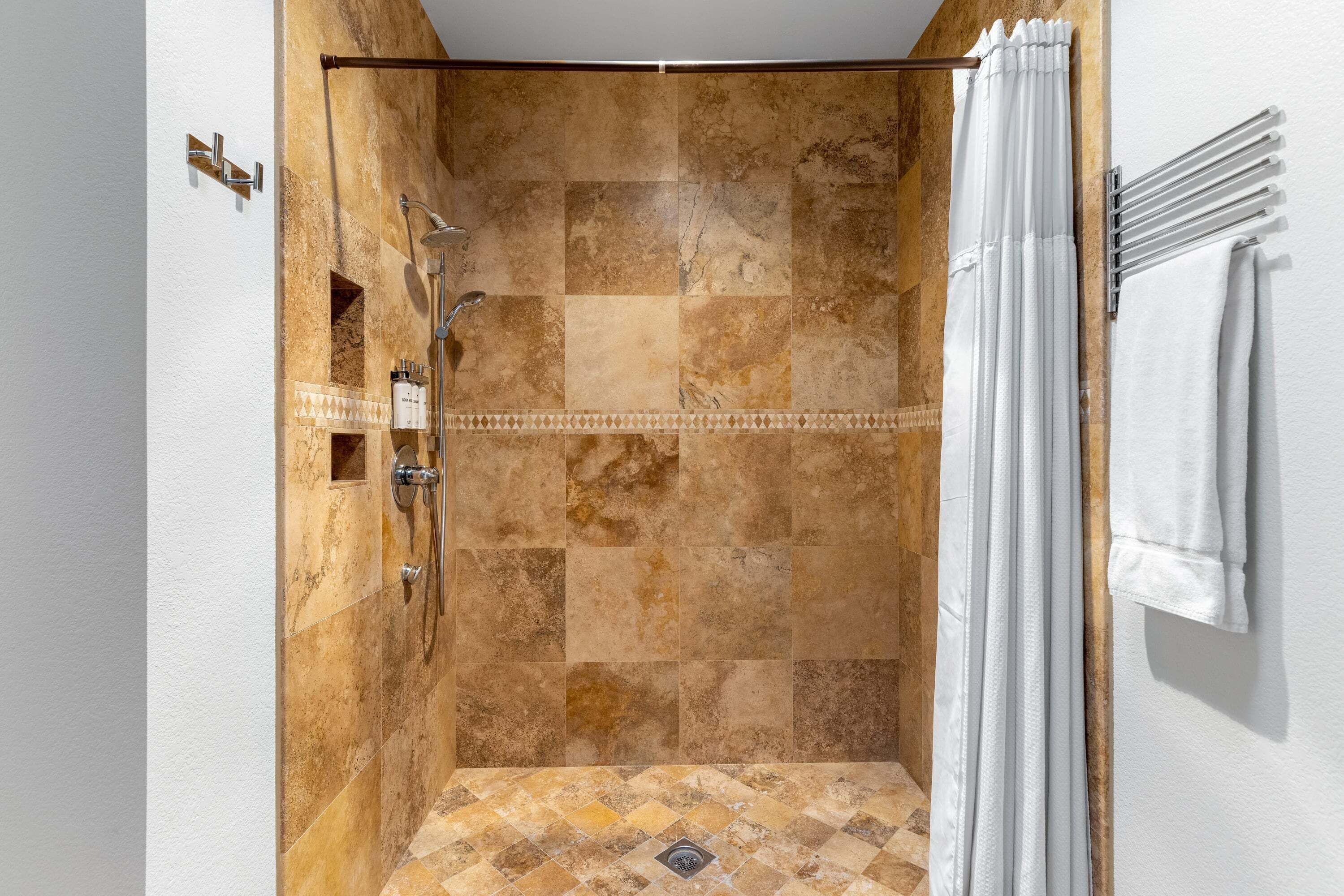 Un espacio de ducha con suelo de baldosas, un cabezal de ducha y una cortina.