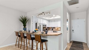 Una cocina moderna con armarios blancos, encimera de granito y una isla central con taburetes de bar.