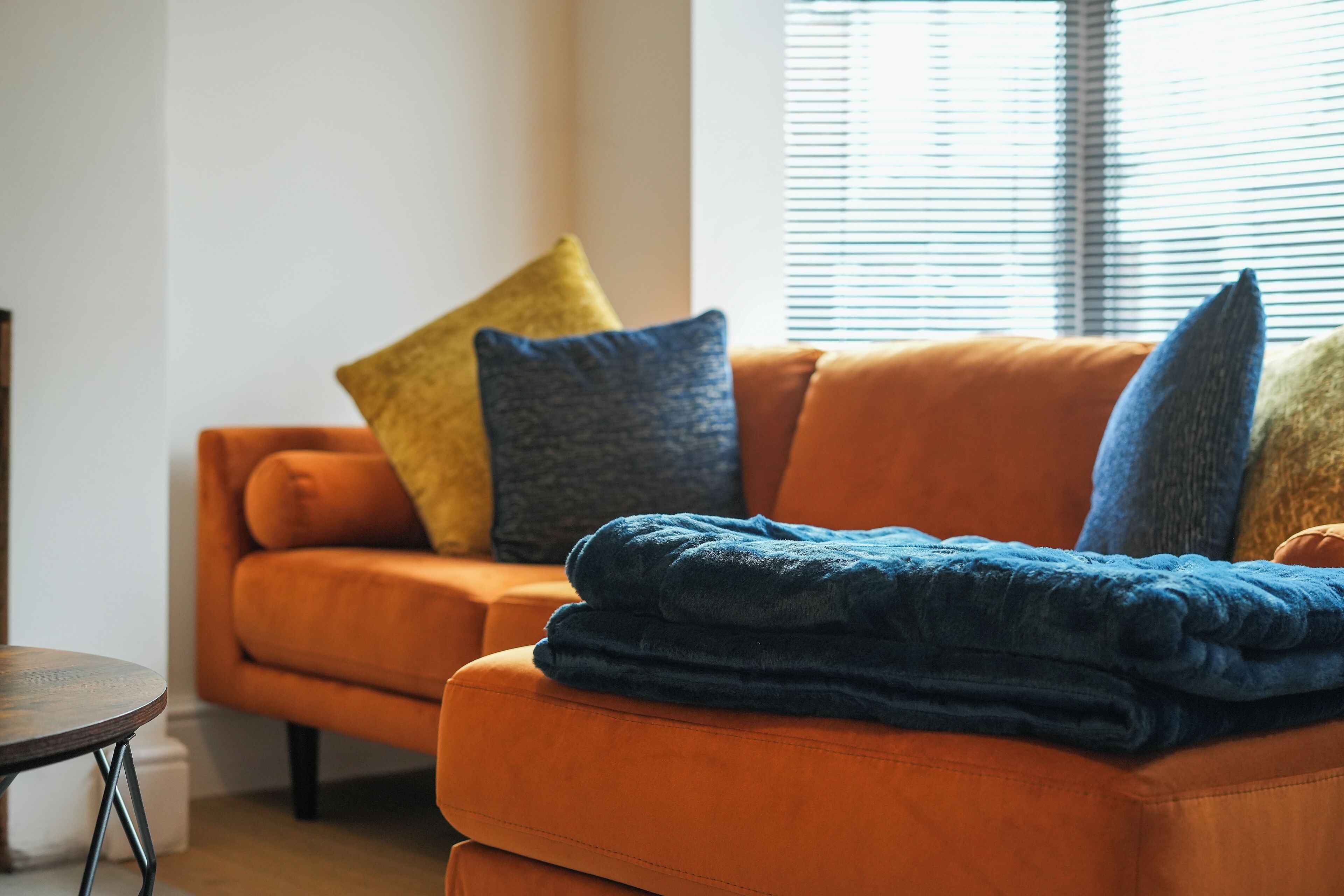 A living room with an orange sofa, a blue blanket, and a yellow pillow.
