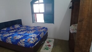 A bedroom with a bed, a window, a wooden door, and a small stool. - Fresh breeze.  In front of the sea (Barra Velha)