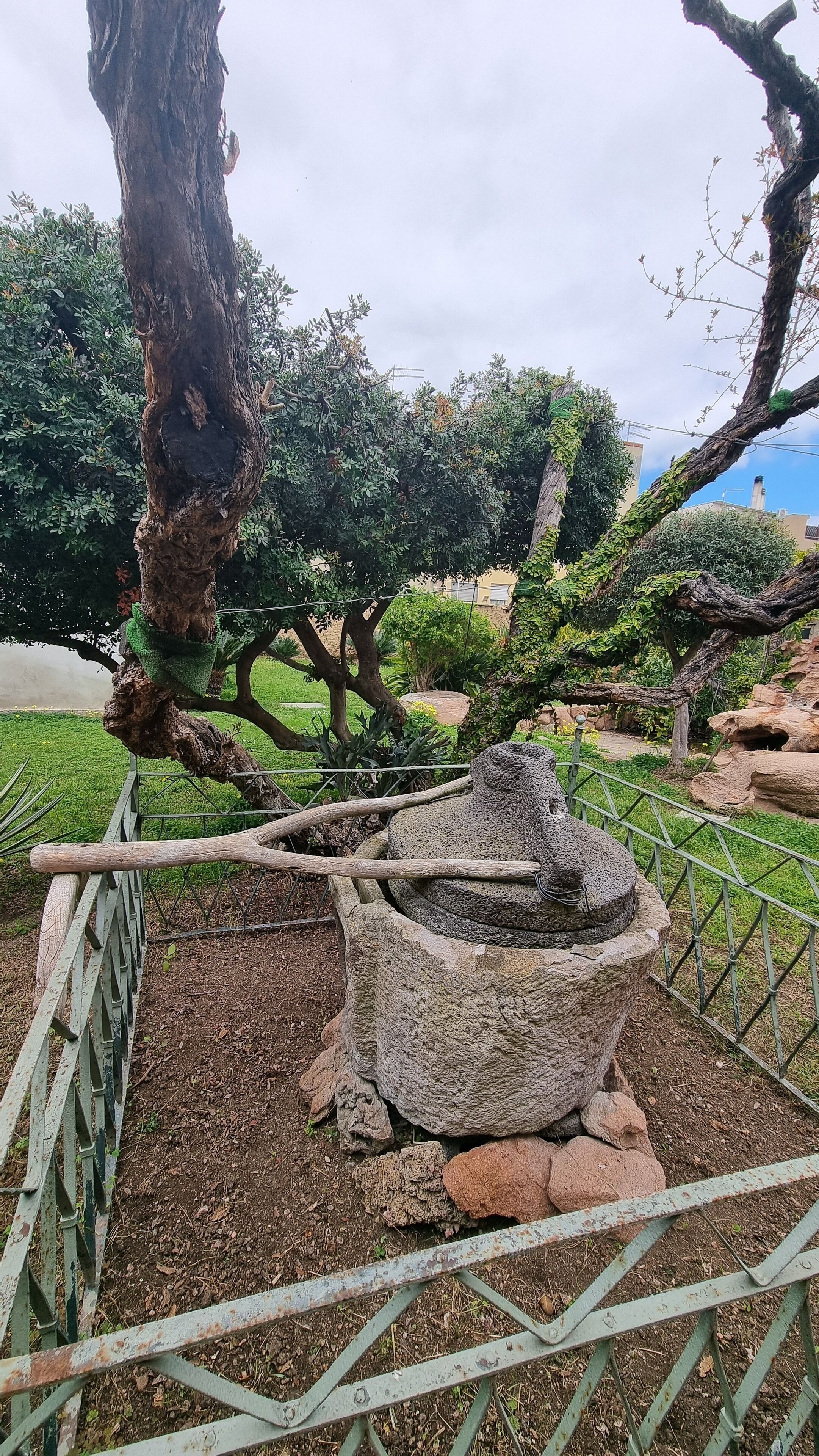 Un jardín con un árbol grande, una estructura de piedra y una valla de metal.