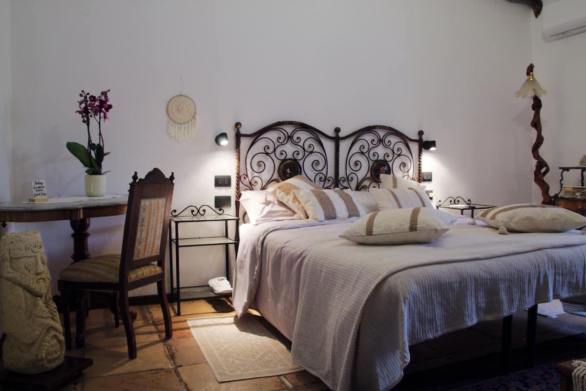 A bedroom with a bed, a chair, a desk, and a wall-mounted shelf.