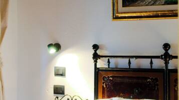 A neatly made bed with a headboard, a wall-mounted light, and a framed painting above it.