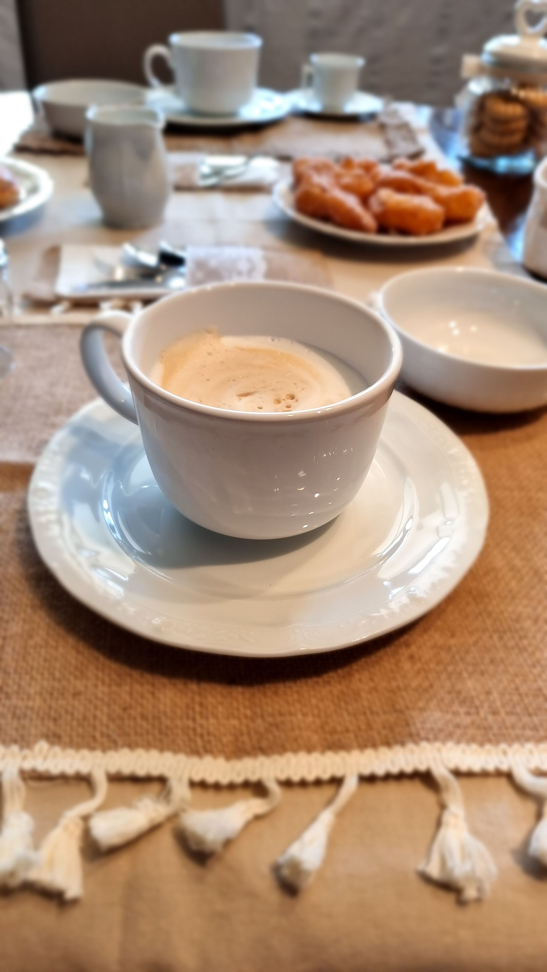 Eine Tasse Kaffee auf einem Untertasse mit einem Tablett Gebäck im Hintergrund.