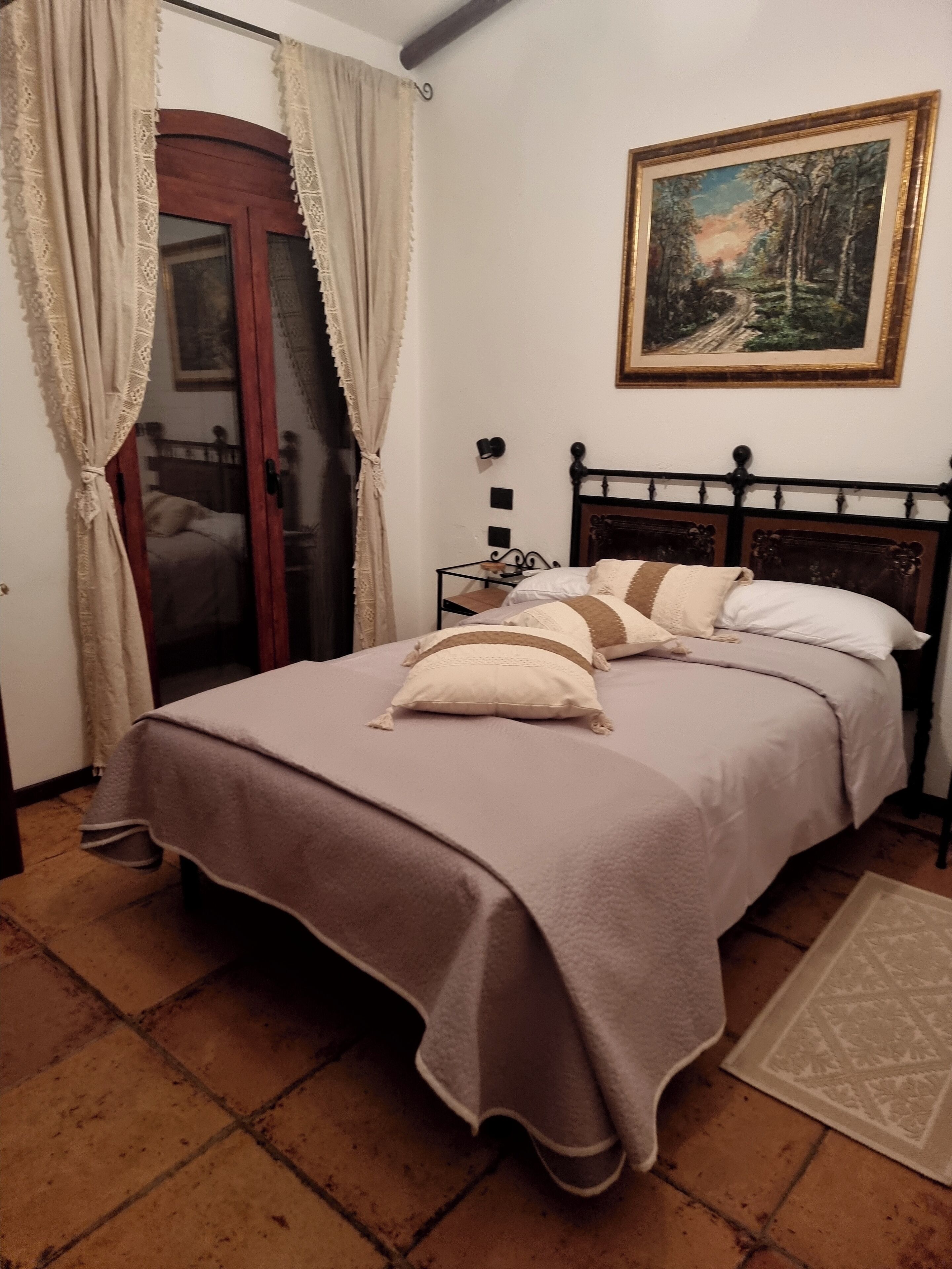 A bedroom with a bed, curtains, a painting, and a tiled floor.