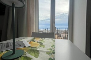 A room with a table, a chair, and a window with a view of buildings and a railing. - 🌊 Exclusive ocean view in the heart of Salerno (Salerno)
