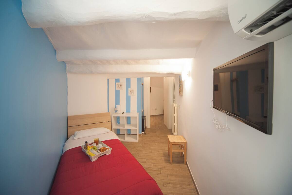 A small, neatly arranged bedroom with a single bed, a bedside table, and a TV mounted on the wall.