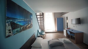 A modern hotel room with a large cityscape painting, a bed with white linens, a desk with a chair, and a TV mounted on the wall. - Home Salvator Rosa 78  (Naples)